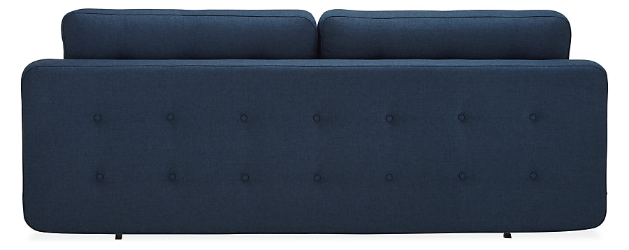 Rear perspective of the Deco Convertible Sleeper Sofa, showcasing its modern, tufted design in a dark blue hue. This sofa boasts a sleek and minimalist form with two cushions lining the top and petite legs for an elegant appearance.