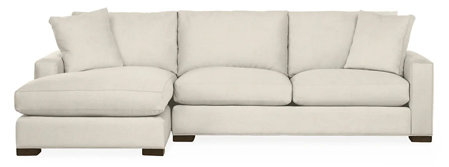 The Metro Sofas with Chaise is a spacious, light beige sectional featuring a left-sided chaise. It boasts thick cushions and rests on short, dark wooden legs, with an array of matching cushions along the back.