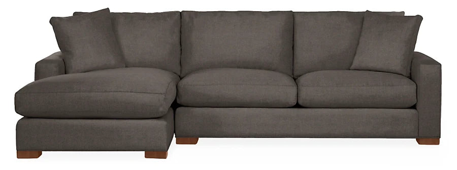 The Metro Sofas with Chaise is a dark gray sectional featuring clean lines and generously padded cushions. Designed with a left-side chaise lounge, it creates a cozy and modern seating area, supported by wooden block feet.