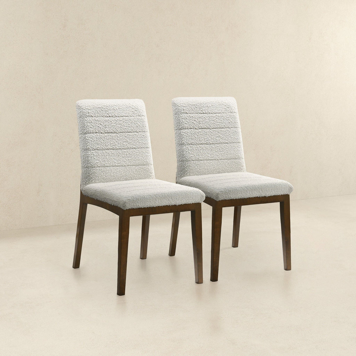 The Ines Modern Dining Chairs, set of 2, feature light-colored fabric upholstery and dark wooden legs. Arranged side by side against a beige background, they showcase a sleek design with horizontally stitched patterns on the backrest.