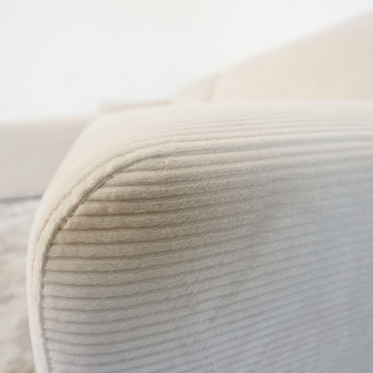 The Mar High-Quality Sectional Sofa features a close-up of its cream-colored ribbed fabric arm, emphasizing its soft texture and rounded design against a blurred background.