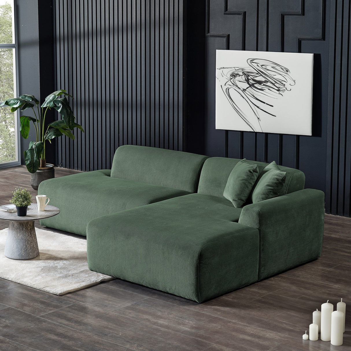A modern living room showcases the Mar High-Quality Sectional Sofa in green, a round table with a plant, and a white abstract painting on a dark paneled wall. Tall windows and potted greenery add natural touches, while candles rest nearby.