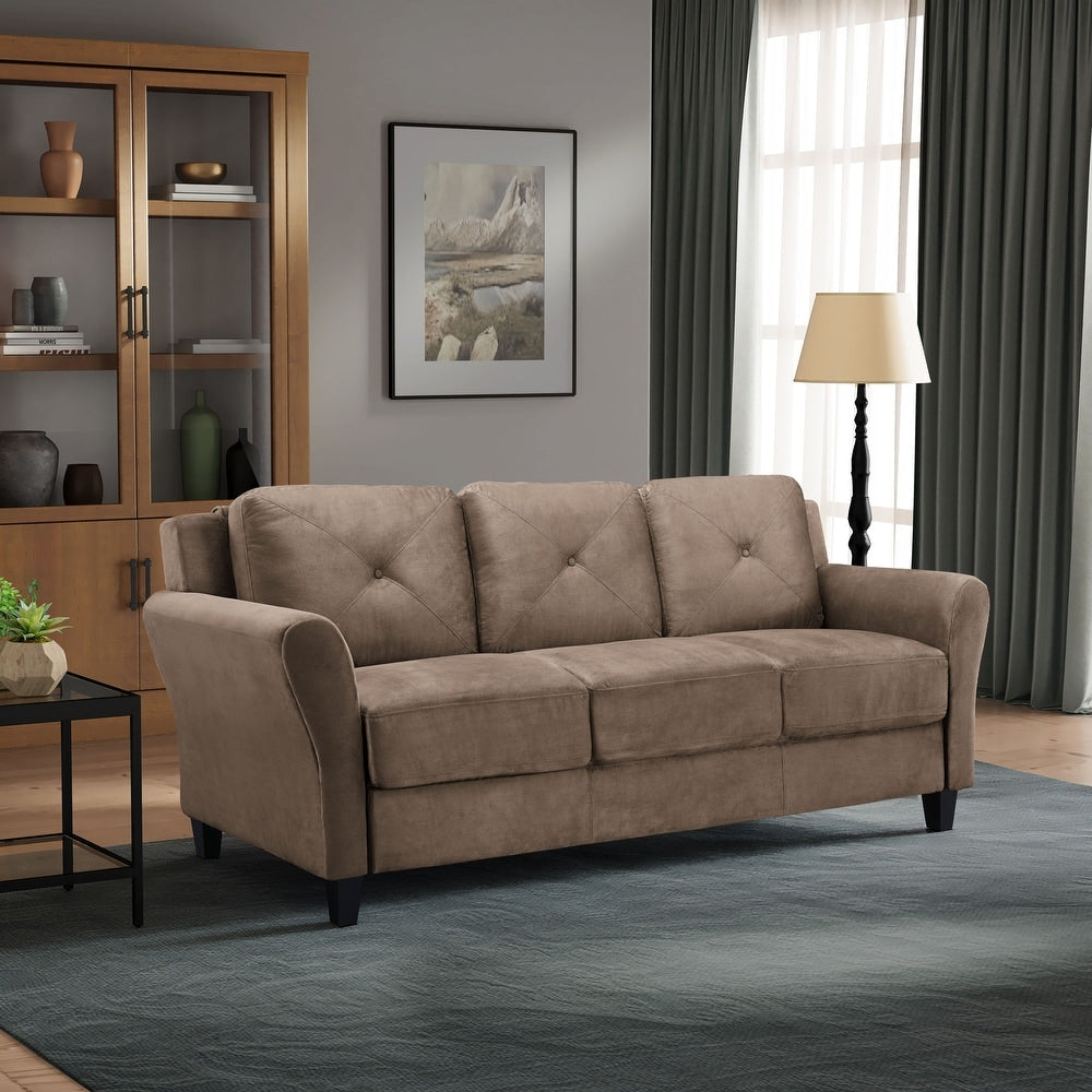 A cozy living room featuring the iLounge Harvard Microfiber Sofa in a rich brown tone sits on a blue rug, complemented by a floor lamp and a window with green curtains. A wooden cabinet and nature painting elegantly adorn the wall.