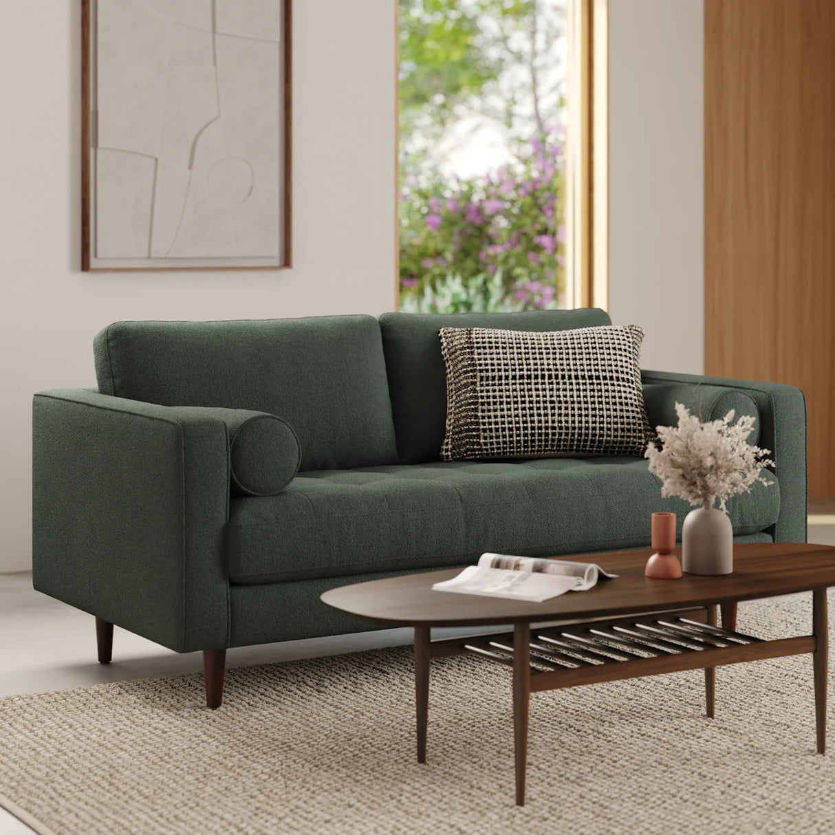 A modern living room featuring the Sven 72 Tufted Loveseat Ratine Oxide, adorned with a dark green cover and paired with a black and white checkered pillow. A wooden coffee table hosts dried flowers and decorative items. The backdrop boasts a large window complemented by abstract wall art.