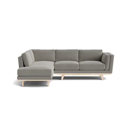 The Kirnik Bumper Sectional in Natural Latex is a modern L-shaped sofa featuring light gray upholstery and light wood legs, beautifully set against a plain white background.