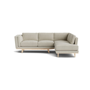 Introducing the Kirnik Bumper Sectional in Natural Latex, an L-shaped sectional sofa on a white background with wooden legs. This piece boasts clean lines and a modern design, complete with plush cushions on both the seats and backrests in a light gray hue.