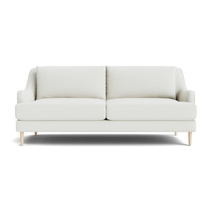 The Kaydan Sofa features a minimalist design in beige, accompanied by two cushions and sleek, light wooden legs, all set against a plain white background.