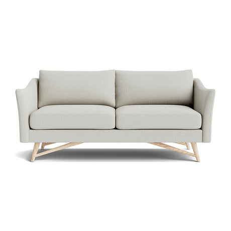 The Gio Sofa in Natural Latex showcases a modern design with its light gray fabric and sleek lines. It features two seat cushions and sits atop a wooden base with angled legs. The sofa's slightly curved armrests contribute to its contemporary and sophisticated look against a white background.