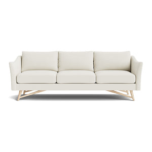 The Gio Sofa in Natural Latex is a modern cream-colored piece, fitted with three cushions and wooden legs. It features angled arms and a minimalist design, all set against a white background.