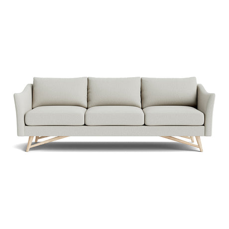 Introducing the Gio Sofa in Natural Latex, a contemporary piece upholstered in light gray fabric with three cushions and angled wooden legs. It boasts gently curved armrests and a sleek design, perfect for modern interiors.