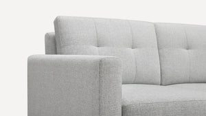 Close-up of the Nomad Fabric Sofa in light gray, showcasing its tufted backrest and sleek, modern lines. The fabric texture is clear, with the image highlighting the armrest and part of the backrest.