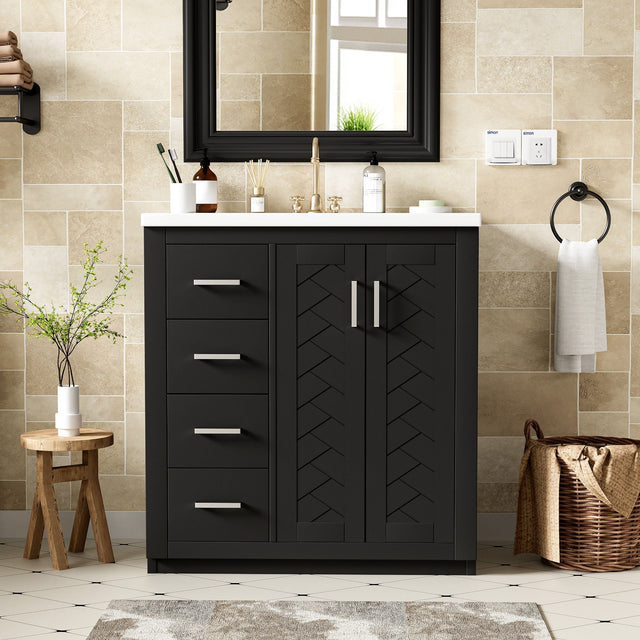 A modern bathroom with beige tile walls features a dark freestanding vanity set including a ceramic sink, three drawers, and soft closing doors. A large mirror hangs above. A wooden stool with a plant and a woven basket are nearby. A hand towel is beside the sink.