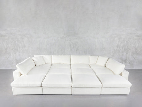 A spacious 12-Seat Deep Modular Daybed with plush cushions and wide seats sits against a light gray textured wall in a minimalist room featuring a concrete floor.