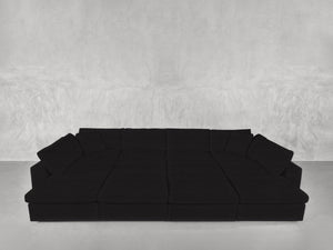A 12-Seat Deep Modular Daybed in black, featuring multiple cushions, is set against a light gray textured wall on a smooth, light-colored floor.