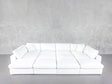 A 12-Seat Deep Modular Daybed with white upholstery and multiple cushions sits against a plain light gray textured wall on a gray floor.