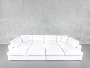 A 12-Seat Deep Modular Daybed with white upholstery and multiple cushions sits against a plain light gray textured wall on a gray floor.