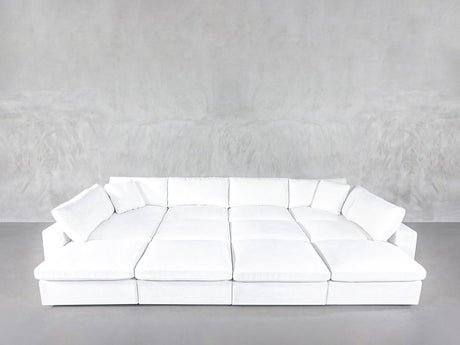 A 12-Seat Deep Modular Daybed with white upholstery and multiple cushions sits against a plain light gray textured wall on a gray floor.