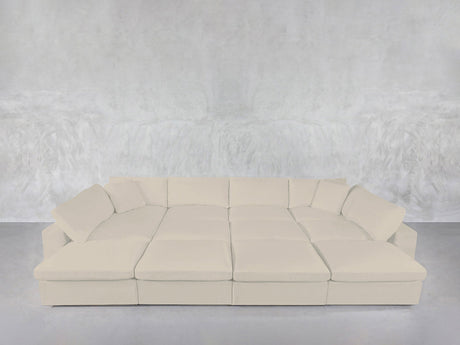 The 12-Seat Deep Modular Daybed, in a modern cream tone with multiple cushions, is arranged against a textured light gray wall and floor for a minimalistic, contemporary vibe.