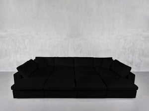 A spacious, modern 12-Seat Deep Modular Daybed with plush cushions sits against a plain light gray textured wall and a smooth, light-colored floor.