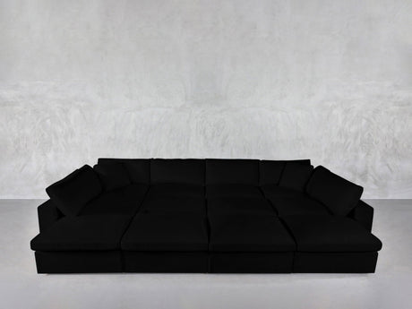 A spacious, modern 12-Seat Deep Modular Daybed with plush cushions sits against a plain light gray textured wall and a smooth, light-colored floor.