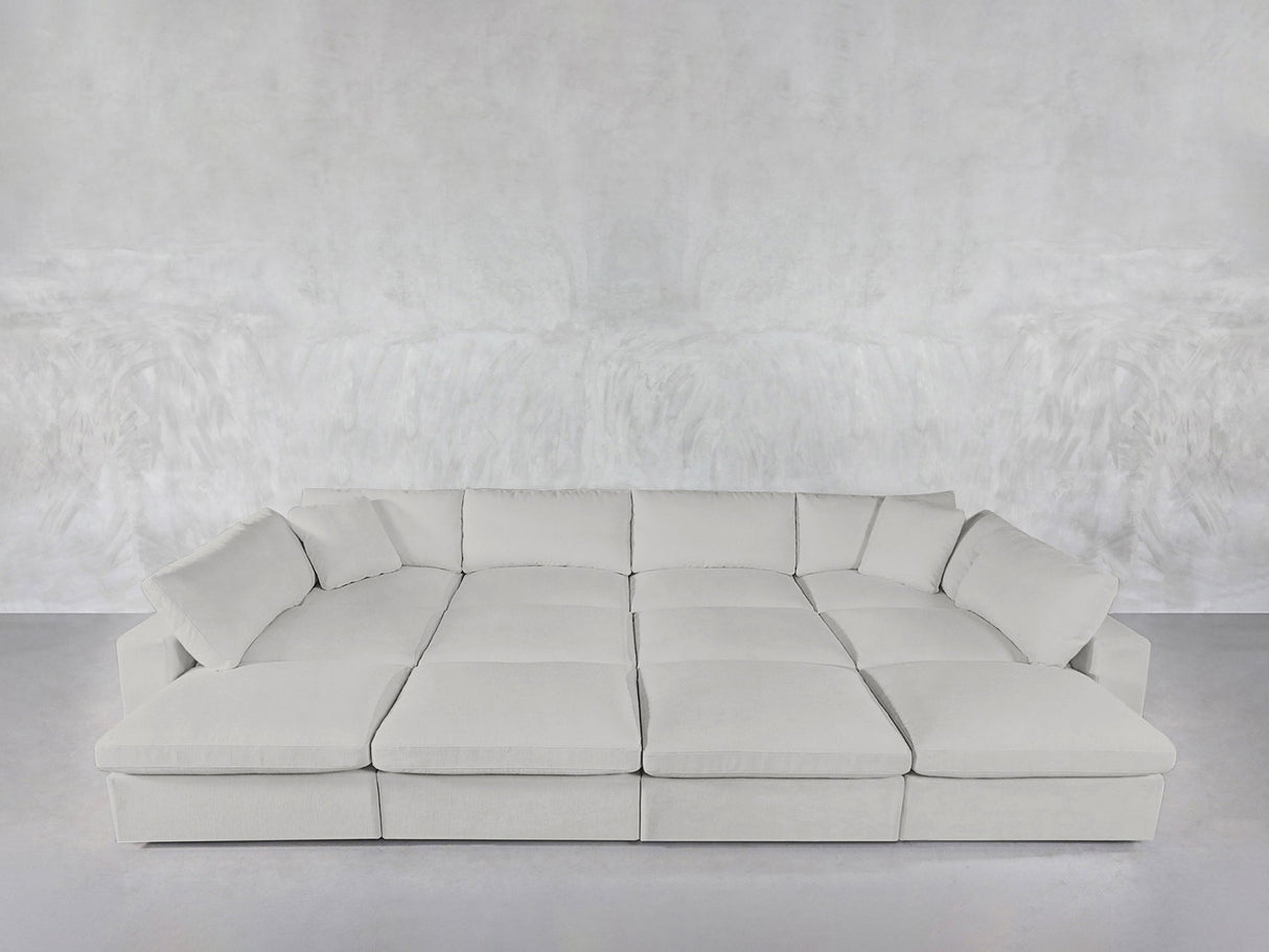 A spacious, modern 12-Seat Deep Modular Daybed with multiple cushions sits against a matching textured gray wall and floor in a minimalist room.