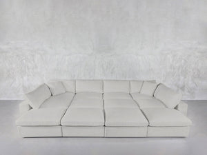 A spacious, modern 12-Seat Deep Modular Daybed with multiple cushions sits against a matching textured gray wall and floor in a minimalist room.