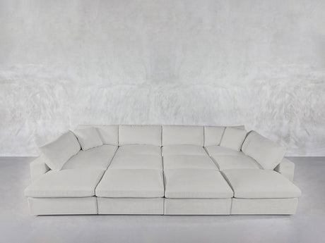 A spacious, modern 12-Seat Deep Modular Daybed with multiple cushions sits against a matching textured gray wall and floor in a minimalist room.