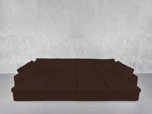 A 12-Seat Deep Modular Daybed in dark brown with multiple cushions is set against a light gray textured wall on a smooth, light-colored floor.