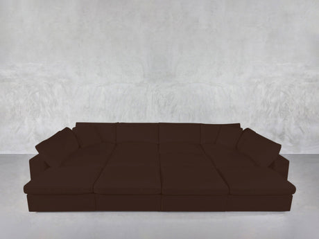 A 12-Seat Deep Modular Daybed in dark brown with multiple cushions is set against a light gray textured wall on a smooth, light-colored floor.