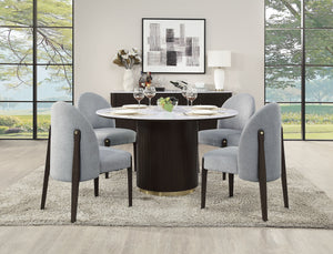 A modern dining room features the Clayten Around Dining Table in Marble/Espresso, set with plates and wine glasses, surrounded by four upholstered chairs. Neutral-toned walls and floors enhance large windows revealing outdoor greenery, abstract wall art, and a decor-adorned sideboard.