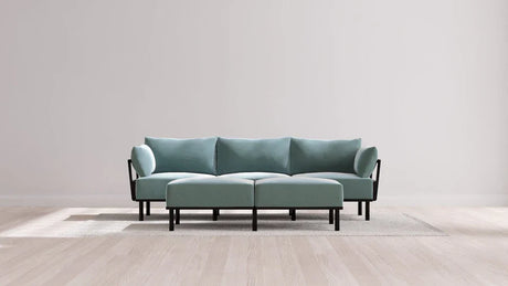 A modern living room with an Indoor Jack 3-Seater Sofa and Bench Ottoman in Balsa resting on a textured rug. The space features a minimalist design with a light wood floor and neutral wall backdrop, creating a clean and serene atmosphere.