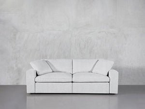 A minimalist room featuring a 2-Seat Modular Loveseat in light gray positioned against a matching textured gray wall. The smooth floor enhances the contemporary decor, creating a calm and neutral ambiance.