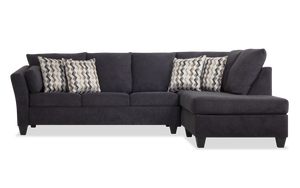 The Virgo Charcoal 119'' 2 Piece Chaise Sectional, with its dark gray hue and right-side chaise section, sits against a white background. It features a clean, modern design and includes five patterned throw pillows showcasing a chevron pattern.