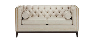 The Anderson Loveseat, in beige with a tufted design and nailhead trim, sits on dark wooden legs. It includes two matching cylindrical bolster pillows on the sides, offering an elegant and sophisticated look.