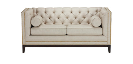 The Anderson Loveseat, in beige with a tufted design and nailhead trim, sits on dark wooden legs. It includes two matching cylindrical bolster pillows on the sides, offering an elegant and sophisticated look.