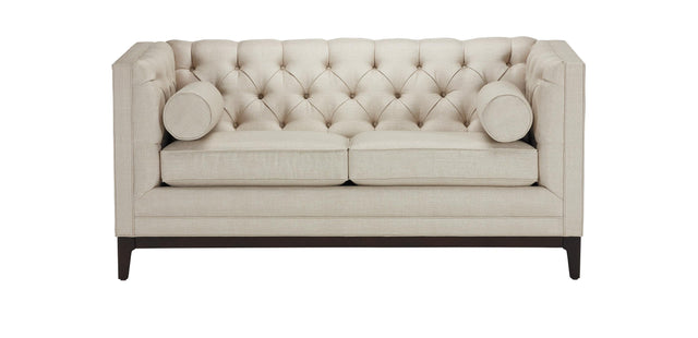 The Anderson Loveseat features a beige tufted design with two seat cushions and two bolster pillows. It has a high back and sides, supported by dark wooden legs.