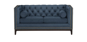 The Anderson Loveseat is a rectangular sofa in dark teal, featuring a tufted design with nailhead trim along the edges. It comes with two seat cushions and two cylindrical bolster pillows, all supported by dark wooden legs.