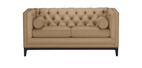The Anderson Loveseat, in a beige hue with tufted upholstery, is showcased against a white background. It includes two cylindrical pillows and is adorned with nailhead trim along the edges, resting on dark wooden legs.