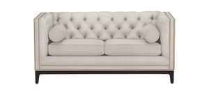The Anderson Loveseat is a beige tufted seat with a high back and sides, accented by nailhead trim. It features two seat cushions and two cylindrical bolster pillows, supported by dark wooden legs.