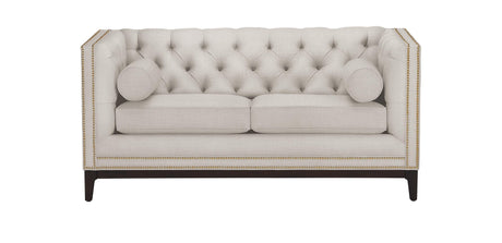 The Anderson Loveseat is a beige tufted seat with a high back and sides, accented by nailhead trim. It features two seat cushions and two cylindrical bolster pillows, supported by dark wooden legs.