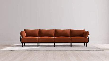 An Indoor Jack 4-Seater Sofa in Balsa with a modern modular design and black metal legs is adorned with four cushions and rests on a light gray carpet. It is set against a plain white wall on a wooden floor.