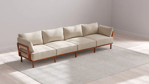 An Indoor Jack 4-Seater Sofa in Balsa is elegantly arranged on a light gray area rug, placed in a sunlit room featuring light-colored hardwood floors and white walls.