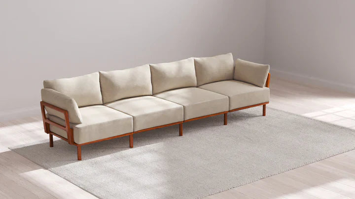 An Indoor Jack 4-Seater Sofa in Balsa is elegantly arranged on a light gray area rug, placed in a sunlit room featuring light-colored hardwood floors and white walls.