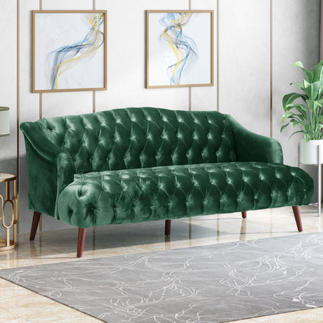 A Comfy 3 Seat Sofa with wooden legs, upholstered in green velvet, enhances a stylish living room featuring light walls, abstract art, a large potted plant, and a subtly patterned gray rug.