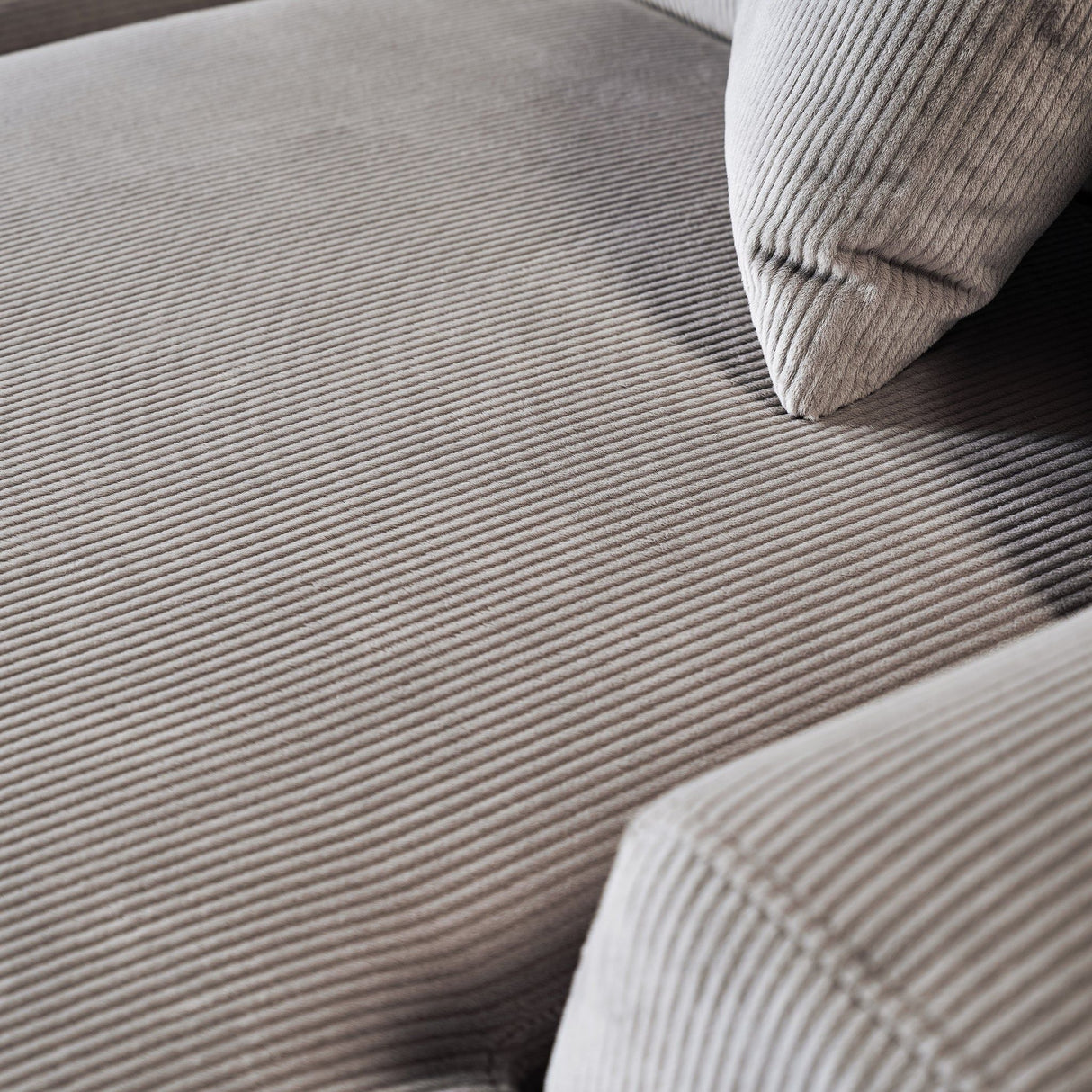 A close-up of the beige corduroy fabric on the Mar - High-Quality Sectional Sofa reveals its soft, ribbed texture, covering the seat cushion and backrest. A matching pillow rests on the sofa, with lighting accentuating its pattern and texture.