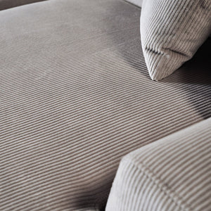 A close-up of the beige corduroy fabric on the Mar - High-Quality Sectional Sofa reveals its soft, ribbed texture, covering the seat cushion and backrest. A matching pillow rests on the sofa, with lighting accentuating its pattern and texture.