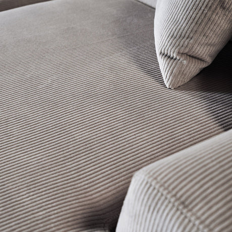 A close-up of the beige corduroy fabric on the Mar - High-Quality Sectional Sofa reveals its soft, ribbed texture, covering the seat cushion and backrest. A matching pillow rests on the sofa, with lighting accentuating its pattern and texture.