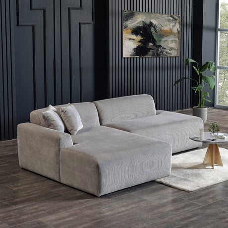 A modern living room features the Mar - High-Quality Sectional Sofa in gray with two cushions on a light area rug. Nearby, a round coffee table holds a plant and book. A potted plant sits by the window, while abstract art adorns the black paneled wall.
