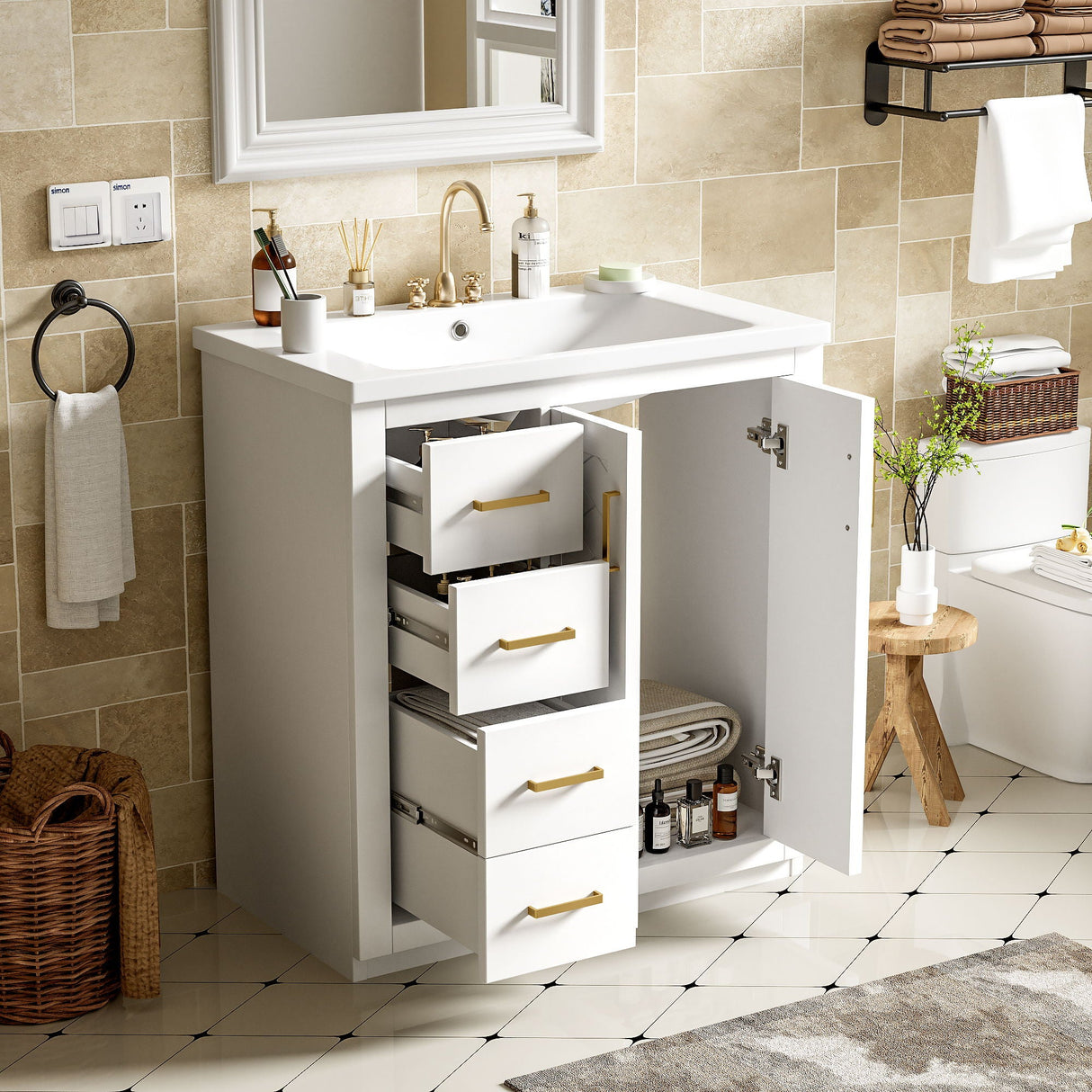 The Ceramic Sink Combo features a freestanding vanity set with white cabinets, gold handles, three drawers displaying toiletries, and soft closing doors revealing towels. Nearby are a basket of towels, a toilet, and a wooden stool against beige tiled walls and floor.