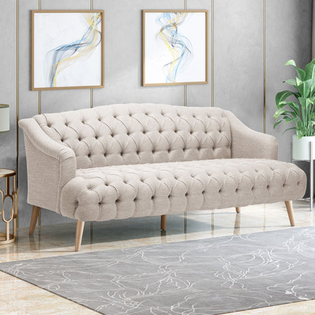 The Comfy 3 Seat Sofa with wooden legs sits on a modern patterned rug. Two abstract paintings with blue and gold accents hang behind, while a green plant in the corner adds a natural touch to the stylish room.